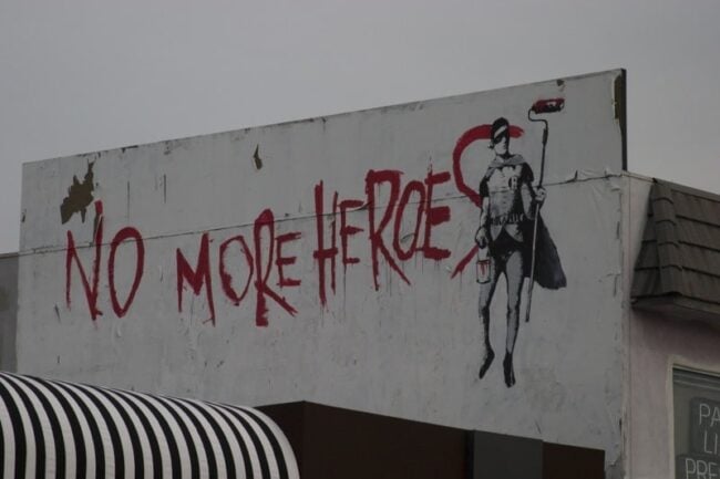 Street mural reading 'No More Heroes' with a stenciled figure holding a paint roller