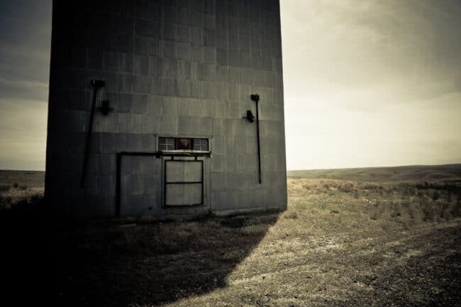 Black and white photo of an old grain elevator building in an open field