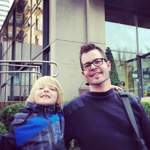 A man wearing glasses standing with a young boy outside a building