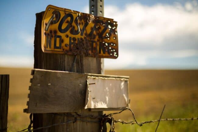 Weathered 'Posted No Hunting' sign nailed to a wooden fence post in an open field