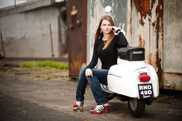 Woman sitting on a white vintage scooter against an industrial backdrop