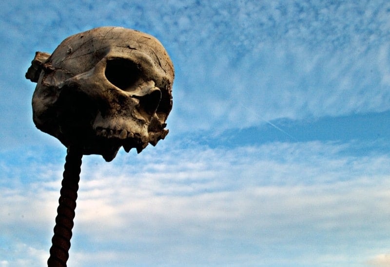 A weathered human skull mounted on a metal rod against a cloudy blue sky