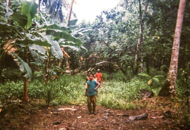 A vintage photo of children standing in a lush tropical jungle clearing with banana leaves and tall trees