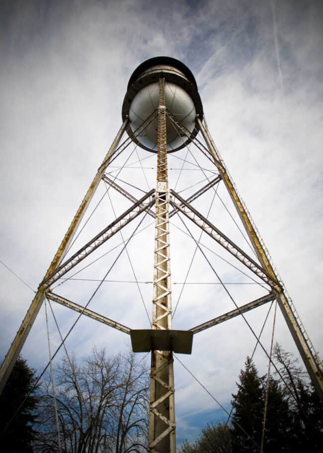 A low-angle view looking straight up at an old steel water tower against a cloudy sky