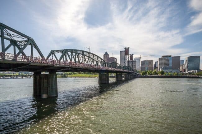 A steel truss bridge crossing a river with the Portland, Oregon skyline in the background