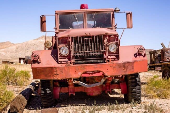 The front of a weathered vintage red truck with a rooftop light, parked in the desert