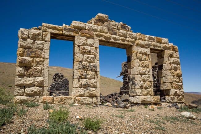 The roofless stone facade of a ruined building with two large window openings, standing alone in the desert
