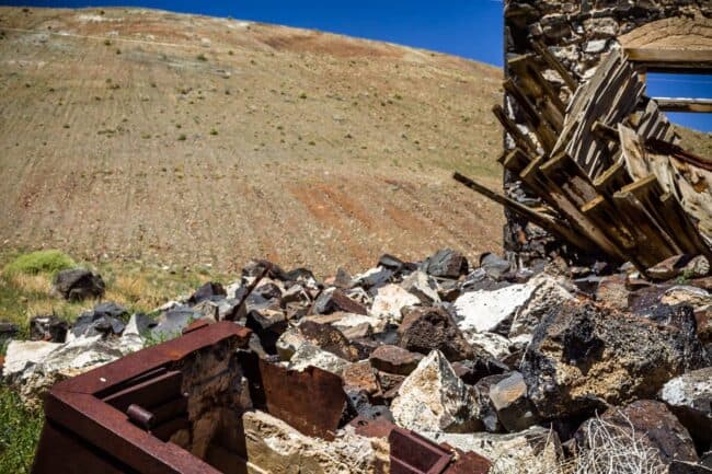 Collapsed wooden roof beams over a stone ruin, with rubble in the foreground against a barren hillside