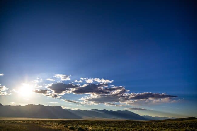 A dramatic desert sunset with sunbeams breaking through clouds over distant mountains