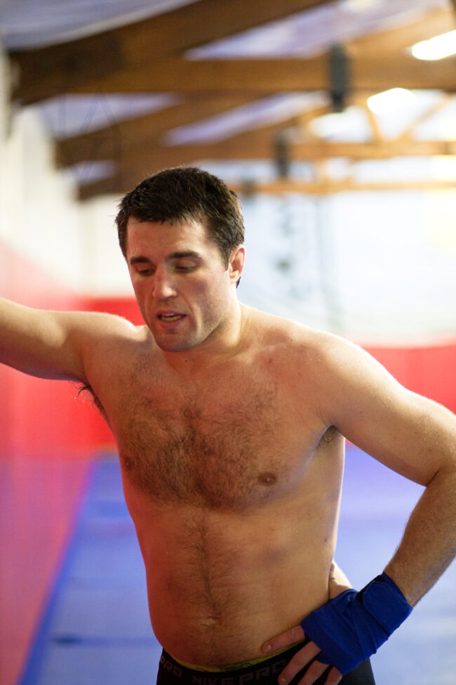 Shirtless male athlete with hand wraps standing in a gym training facility