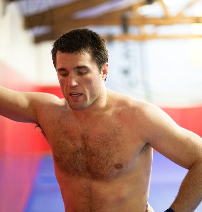 Shirtless male athlete with hand wraps standing in a gym training facility