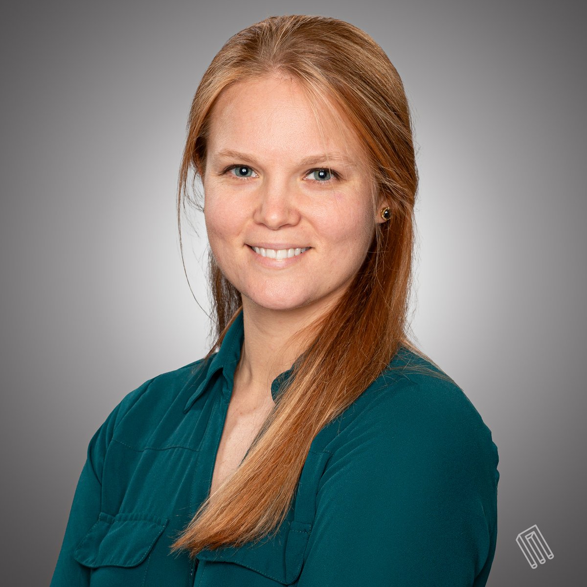 Woman with long reddish-blonde hair smiling in a teal blouse, studio headshot with gray gradient backdrop