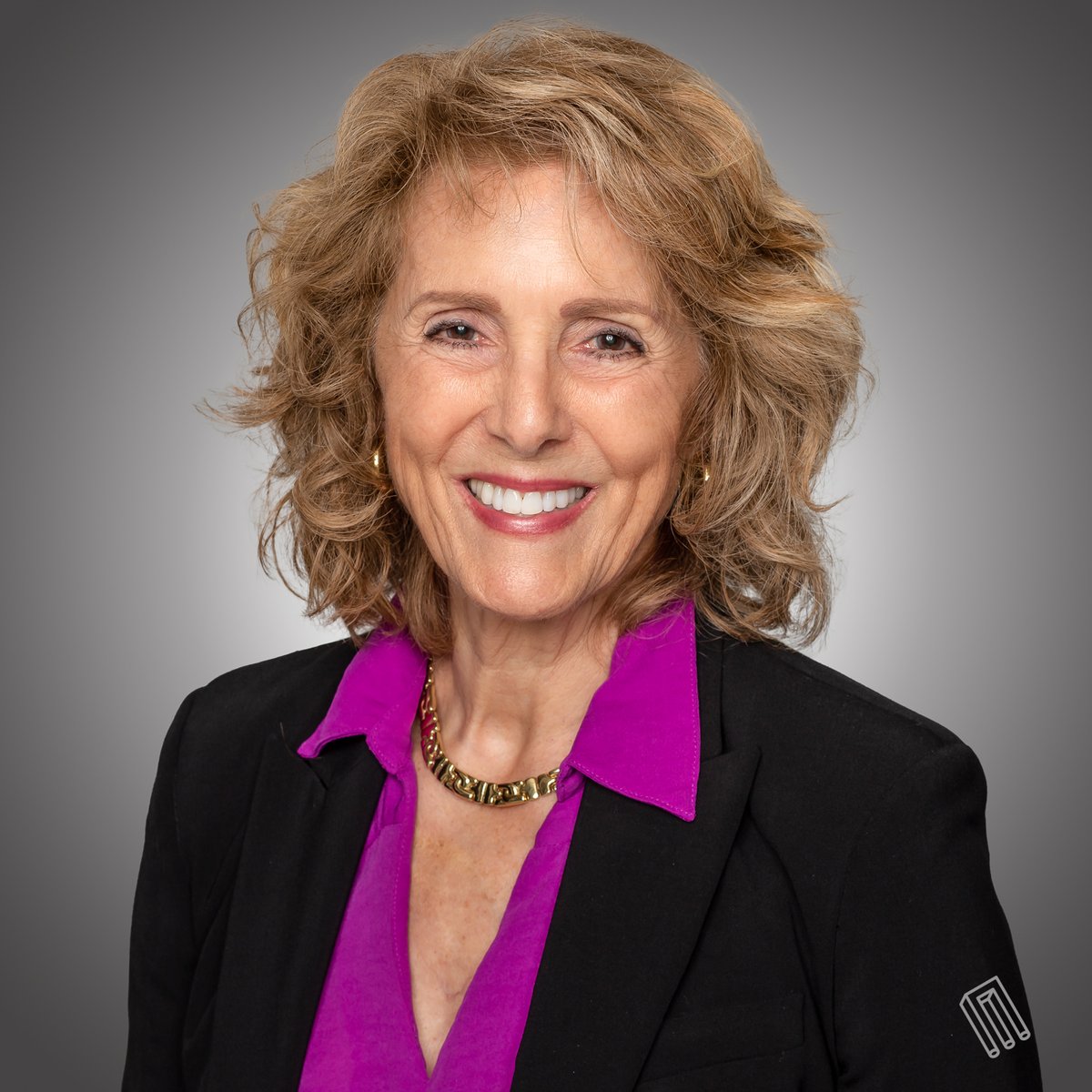 Woman with wavy light brown hair, magenta top, black blazer, gray studio background, color