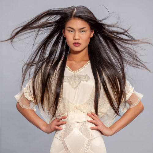 Three-panel editorial triptych of a model with dark hair, dramatic black lipstick, styled in a fashion aesthetic across all three frames, windblown hair, cream dress, lace veil over face