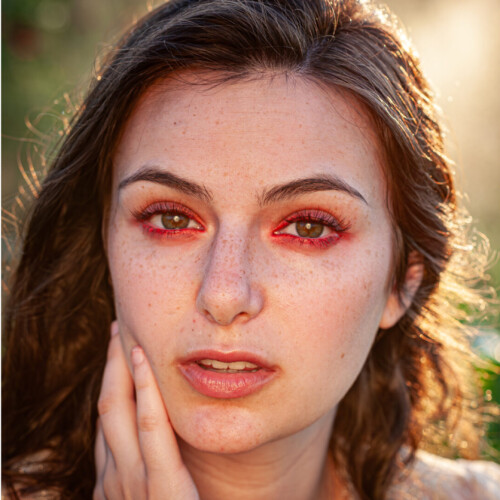 Three-panel triptych of a woman with wavy brown hair and dramatic red eye makeup, posed in three different angles against a rose garden backdrop