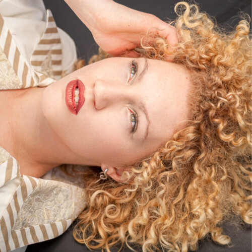 Three-panel triptych of a woman with curly blonde hair and red lipstick in a white-and-gold striped outfit, posed against a vintage car and plain backdrops